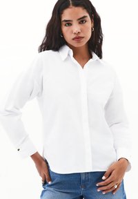 Camisa blanca de botones con mangas largas, cuello clásico y detalles de botones dorados en los puños, fabricada en una tela suave.