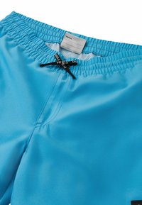 Jasnoniebieskie kąpielówki z elastycznym pasem, czarnym sznurkiem do regulacji i metką wewnątrz. Gładka tekstura z detalami szwów.