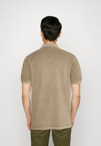 Bruine poloshirt met een kraag en korte mouwen, gemaakt van zachte, gestructureerde stof. Zichtbare stiksels langs de onderkant en de mouwen.