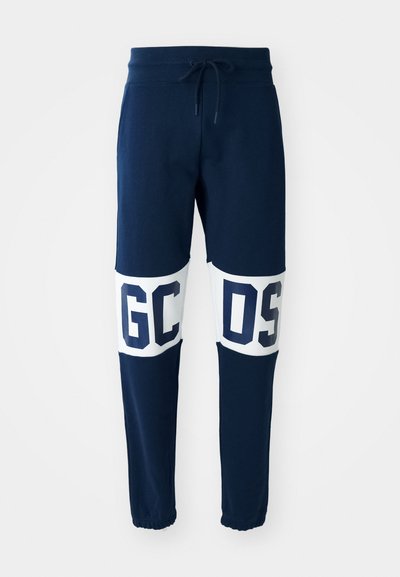 Calças de moletom azul-marinho com cintura elástica e cordão ajustável. Apresenta grandes letras brancas "GC" e "OS" em painéis contrastantes. Torneiras com punhos.