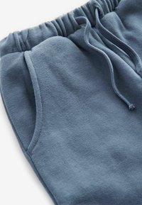 Világoskék jogging nadrág, puha anyagból készült, elasztikus derékkal, zsinórral és oldalsó zsebekkel, amelyek steppelt részletekkel rendelkeznek.