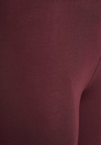 Detailný záber na hladkú, tmavo vínovú látku so subtilnou textúrou a jemným splývaním, ktorý zvýrazňuje detaily materiálu a farby.