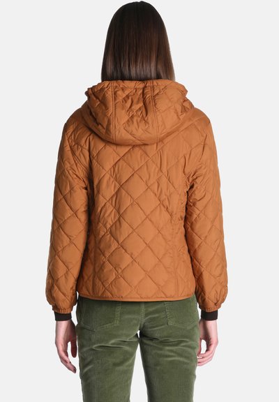 Personne vue de dos portant une veste matelassée marron avec une capuche et un pantalon vert sur un fond clair uni.