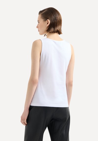 Top senza maniche bianco in cotone, con scollatura tonda e superficie liscia, abbinato a pantaloni di pelle neri.