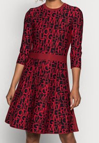 Klänning med röd och svart mönster som har rund halsringning, trekvartslånga ärmar och figursydd midja. Materialet har en strukturerad stickad design.