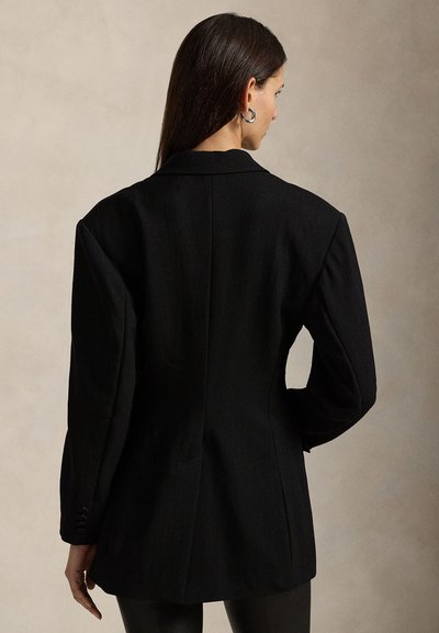 Black blazer with structured shoulders, tailored fit, single-breasted design, and textured fabric. Notable back seam detail and buttoned cuffs.