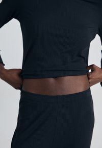 Svart ribbad långärmad topp med figurnära design, parat med matchande ribbade byxor. Båda har en mjuk textur och elastisk midja.