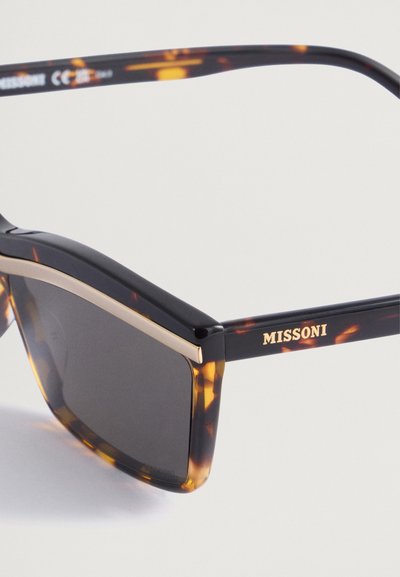Sunglasses iz zloženko iz želvove školjke z velikanskimi kvadratnimi okvirji. Imajo zlati naglas vzdolž vrha in logotip "MISSONI" na ročaju. Temna leča.