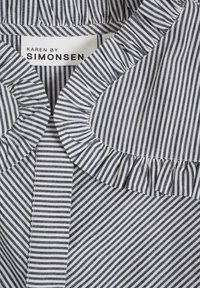 Gestreepte stof in marineblauw en wit met een ruches-kraag. Het label zegt "KAREN BY SIMONSEN." De textuur is glad, met een geweven patroon.