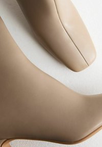 Beige enkelboots van glad leer, met een ronde neus en stikseldetails, een slanke silhouet en minimale ontwerpelementen.