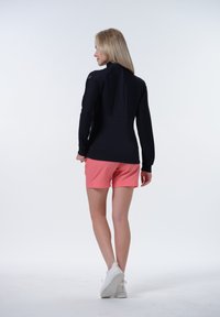 Svart långärmad topp med texturerade axlar, kombinerad med rosa shorts. Outfiten har ett ryggslits och kompletteras av vita sneakers.