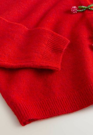Red knit sweater detail featuring ribbed cuffs and hem, with a smooth texture and a decorative beaded accent on the neckline.