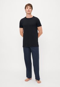 Zwarte t-shirt met korte mouwen gecombineerd met nachtpants in marineblauw met strepen. De t-shirt heeft een eenvoudig ontwerp; de broek heeft verticale witte strepen.