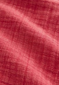 Tissu texturé dans une riche couleur corail, affichant un tissage doux et respirant avec des variations subtiles et une apparence légèrement froissée.