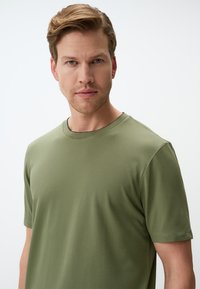 Oliwkowa koszulka z krótkim rękawem z okrągłym dekoltem, o gładkiej fakturze i minimalistycznym wzornictwie, z lekko dopasowanym krojem.