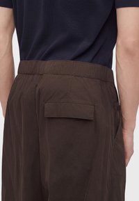 Vue de dos d'une personne portant un pantalon marron foncé avec une poche à rabat et une taille élastique, associée à une chemise à manches courtes bleu marine foncé.