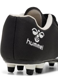 Zwarte voetbalschoenen met een textuur, voorzien van een wit "hummel" logo en contrasterende witte accenten op de kraag. Zwarte rubberen noppen.