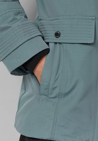 Svijetloplava jakna s rebrastim manžetama i dugmetom, s bočnom džepom i glatkim, teksturiranim materijalom.