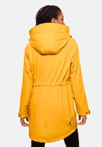 Yellow waterproof jacket with a hood, cinched waist, and snap button cuffs. Features a logo patch near the hem and smooth texture.