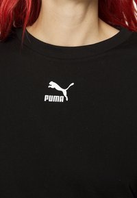 Černé bavlněné tričko s kulatým výstřihem, na kterém je na hrudi potisk bílého loga PUMA a skákající kočky.