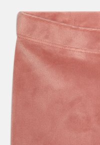 Tessuto di velluto rosa e morbido con una superficie liscia. Presenta una vita piegata con cuciture ordinate per una finitura pulita.