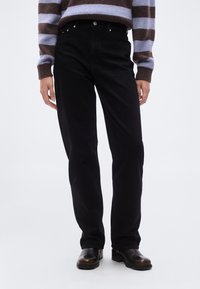 Μαύρα τζιν από denim με κανονική γραμμή στα πόδια, που διαθέτουν μπροστινές τσέπες και κούμπωμα με κουμπί. Φορεμένα με ριγωτό πλεκτό πουλόβερ και μπότες.