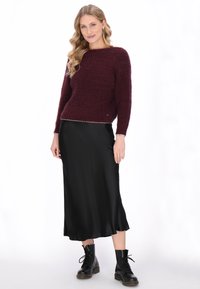 Bordeaux gebreide trui met een gestructureerde afwerking, gecombineerd met een zwarte satijnen midi-rok en zwarte veterschoenen tot de enkel.