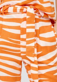 Oranje en wit gestreepte stof met een taillebanddetail, voorzien van een ontspannen pasvorm en zakken. Zachte textuur en lichtgewicht ontwerp.