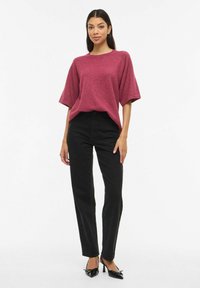 Bordo krāsas pārizmēra džemperis ar īsām piedurknēm, kombinēts ar melnām taisna piegriezuma biksēm ar augstu jostasvietu un melniem kurpju papēžiem ar smailu purngalu.