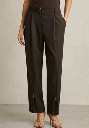 Bruine geplooide broek met een brede tailleband en zijzakken, voorzien van ritsen aan de onderzijde. Het materiaal lijkt glad en lichtgewicht.