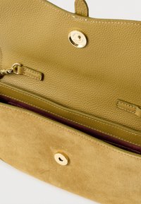 Zelená kožená kabelka se semišovým povrchem, zlatým kováním a magnetickým zapínáním. Uvnitř je kapsa na zip a vínové podšívka.