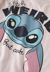 Sweatshirt rose clair avec un grand graphique d'un personnage bleu aux grands yeux. Le personnage a des accents roses brillants et du texte en dessous.