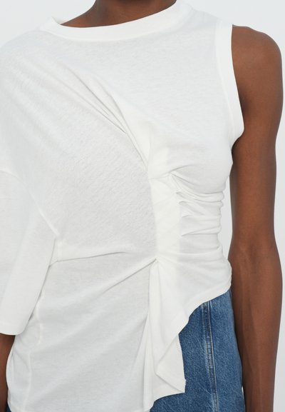 Biela bezrukávová blúzka s nariasenou textúrou na jednej strane, so zaobleným výstrihom a jemnou, ľahkou látkou.