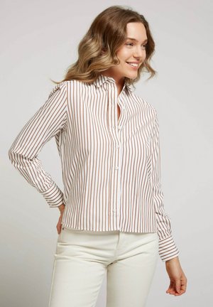 Chemise blanche avec de fines rayures verticales marron, design à boutons, manches longues avec poignets à boutons, et un ourlet légèrement arrondi.