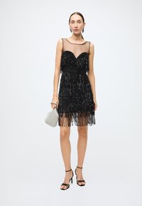 Black sequin dress with fringed hem, sheer neckline, and fitted bodice. Paired with a silver clutch and black strappy heels.