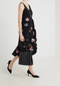 Abito floreale nero con stampe rosa e blu, corsetto aderente, gonna ampia, abbinato a una borsa a tracolla nera e décolleté nere a punta.