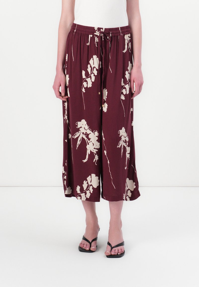 Burgundy culotte pants with cream floral pattern, elastic waistband with drawstring, and wide legs. Paired with black flip-flops.