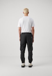 Pantaloni cargo neri con elastico in vita, tessuto testurizzato e tasche laterali. Indossati con una maglietta bianca semplice e scarpe robuste.