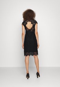 Černé krajkové šaty se zvlněným lemem, krátkými rukávy a hlubokým výstřihem na zádech. Šaty mají složité květinové vzory a přiléhavý střih.