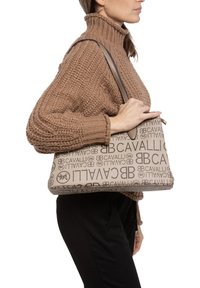 Bruine handtas met patroon, met een tan basis en herhaalde logo-afdrukken, een platte vorm en een enkele schouderriem.