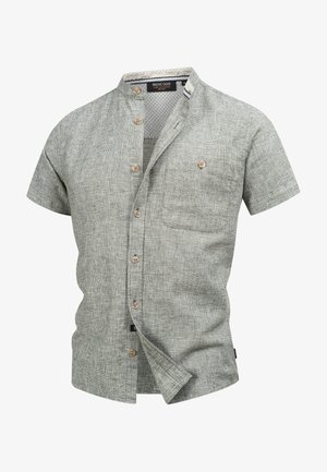 Chemise à manches courtes en tissu texturé de couleur gris clair avec un motif à carreaux et des boutons en bois. Elle possède un col montant et une poche poitrine.