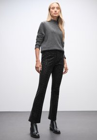 Maglione grigio a collo alto abbinato a pantaloni in velluto nero con stampa leopardata e stivaletti neri con tacco spesso, su uno sfondo neutro.