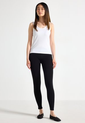 Canotta bianca a coste abbinata a leggings neri. L'outfit presenta un design aderente e una texture morbida, con colori semplici e uniformi.
