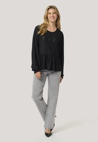 Black peplum top with long sleeves and lace-like pattern. Paired with light gray straight-leg jeans and black heels. Smooth fabric texture.