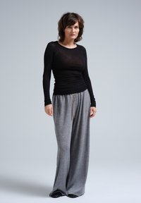 Schwarzes Langarmoberteil in enger Passform mit weicher Textur sowie graue, locker sitzende Sweatpants mit einem Kordelzugbund. Beide Kleidungsstücke sind lässig.