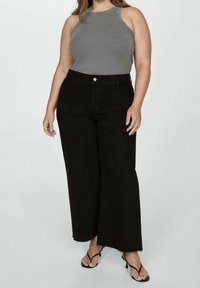 Vaqueros anchos negros con un dobladillo deshilachado, combinados con una camiseta sin mangas gris de corte ajustado y acanalado. La tela parece suave con un ajuste entallado.