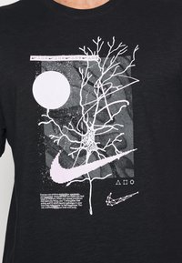 Svart bomullst-shirt med en vit grafisk bild av en trädgren, en cirkel och Nike-märke. Texten nedanför lyfter fram hälsofördelar med träning.