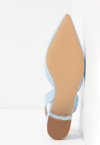 Chaussure plate bleue à bout pointu vue par la semelle, avec une semelle lisse couleur beige, un petit talon et une zone de grip texturée.