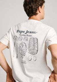 Balta medvilninė marškinėliai su piešiniais ant nugaros: morkos, salotos, kepta mėsa ir kiaušiniai, viršuje esantis užrašas "Pepe Jeans" ir apačioje "Sunday Roast".