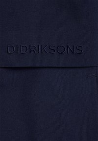 Tissu bleu marine foncé avec "DIDRIKSONS" brodé en fil assorti sur un rabat horizontal ou une zone de poche.